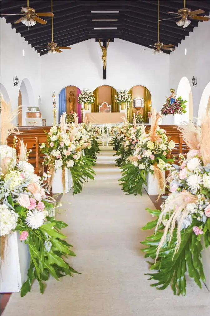 Pasillo de iglesia decorado con arreglos de flores blancas y verdes